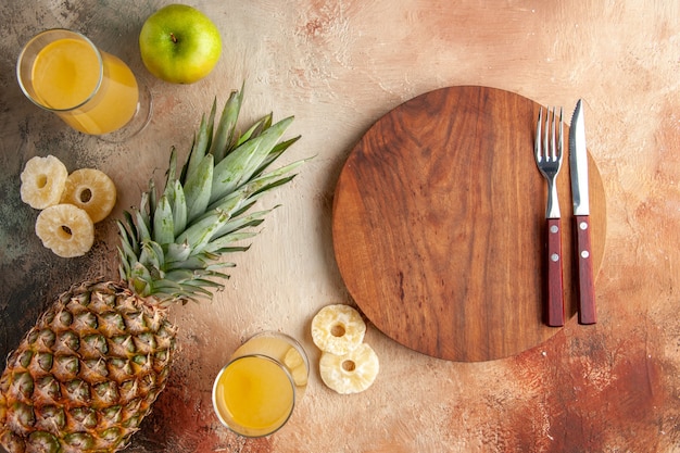 vue de dessus jus d'ananas frais dans des verres fourchette et couteau pomme sur planche de bois sur fond beige