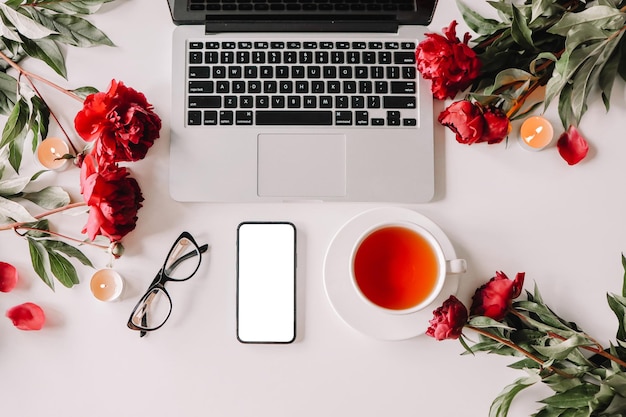 Vue de dessus des lunettes et des fleurs pour ordinateur portable de téléphone portable sur le bureau blanc