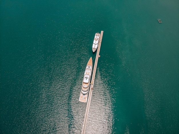 Vue de dessus des luxueux yachts blancs amarrés au long quai mince, mer bleue par une journée ensoleillée ; concept de millionnaire.