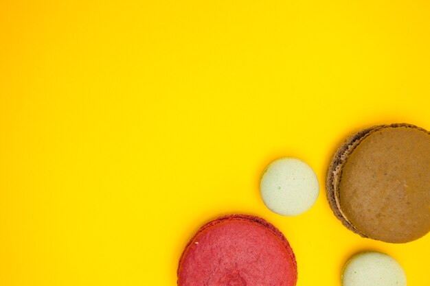 Vue de dessus des macroons de différentes saveurs sur fond jaune. Dessert sucré