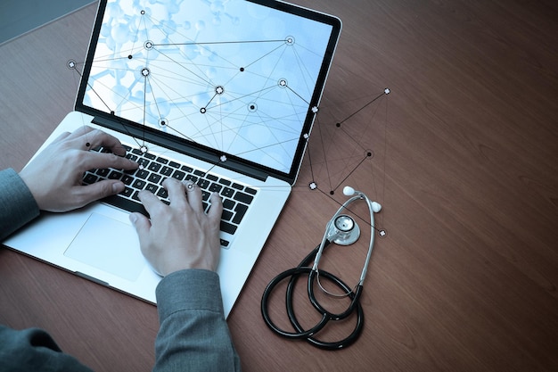 Vue de dessus de la main du docteur en médecine travaillant avec un ordinateur moderne et un téléphone intelligent sur un bureau en bois