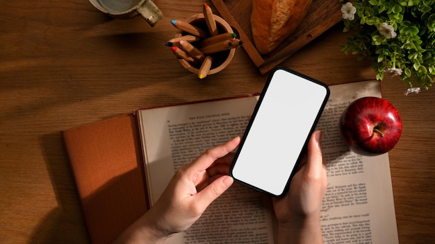 Vue de dessus d'une main féminine tenant un écran vide de smartphone sur une table de lecture
