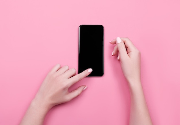 Vue de dessus d'une main de femme à l'aide de téléphone sur fond pastel rose