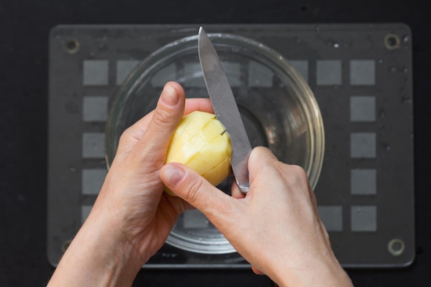 Vue de dessus de la main de femme coupant la pomme de terre crue sur le fond noir