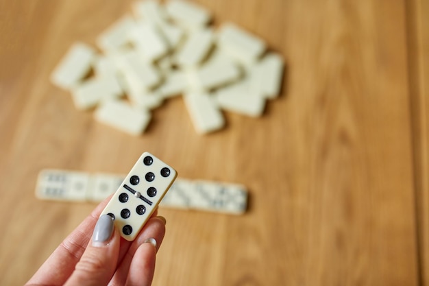 Vue de dessus de la main de la femme jouer à des jeux de dominos blancs sur fond de table en bois avec concept de jeu de société espace copie