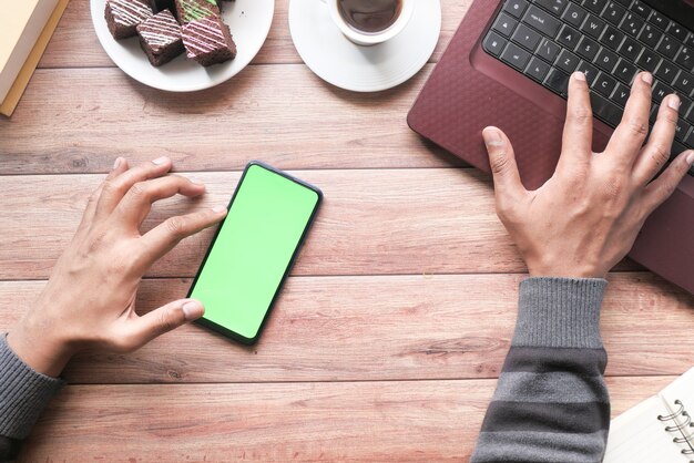 Vue de dessus de la main de l'homme à l'aide d'un téléphone intelligent et en tapant sur un ordinateur portable