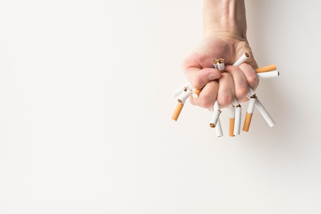 Vue de dessus de la main d&#39;une personne tenant des cigarettes cassées sur fond blanc
