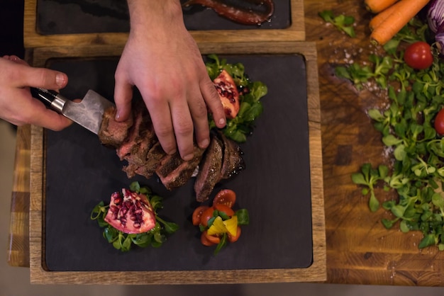 vue de dessus des mains du chef dans la cuisine de l'hôtel ou du restaurant préparant un steak de boeuf avec une décoration végétale