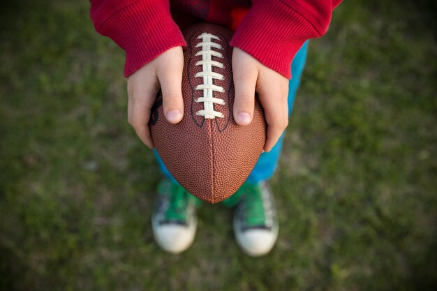 Vue de dessus sur les mains du petit garçon tenant le football sur le stade par une journée ensoleillée