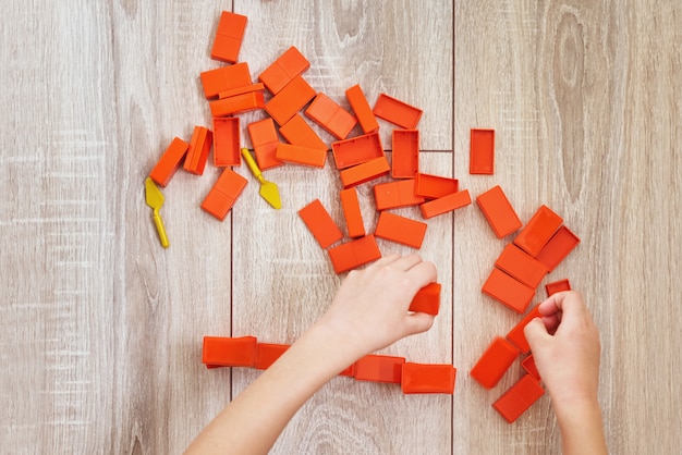 Photo vue de dessus des mains d'enfant jouant avec des briques de jouet orange. concept d'enfants lerning et éducation. loisirs bébé avec jouets en développement