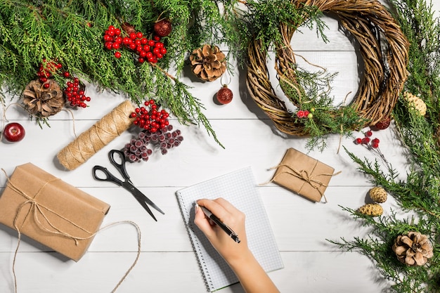 Vue de dessus des mains féminines envelopper des cadeaux emballés pour le nouvel an et faire défiler des branches d'épinette et des outils sur...