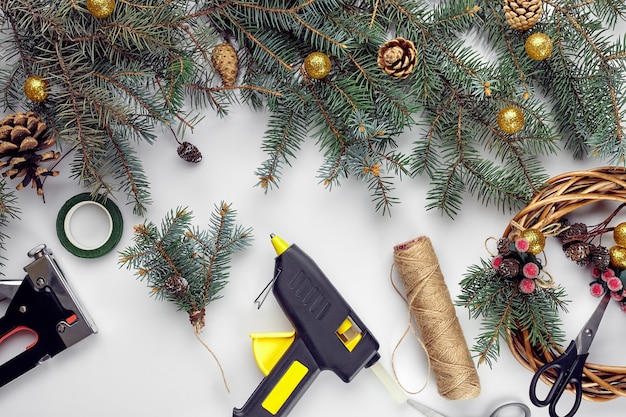 La vue de dessus des mains féminines fait une couronne de Noël emballée des cadeaux et fait défiler des branches et des outils d'épinette ...