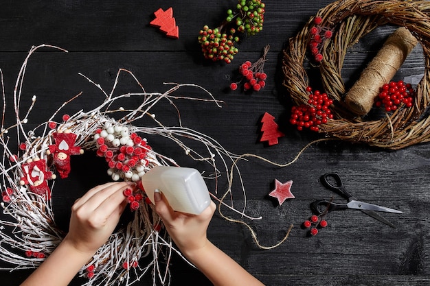 La vue de dessus des mains féminines fait une couronne de Noël emballée des cadeaux et fait défiler des branches et des outils d'épinette ...