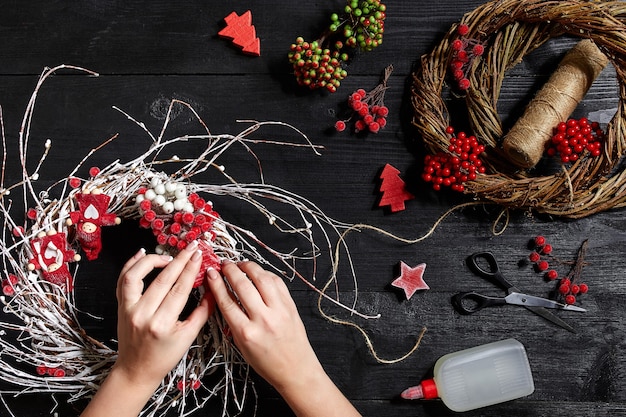 La vue de dessus des mains féminines fait une couronne de Noël emballée des cadeaux et fait défiler des branches et des outils d'épinette ...