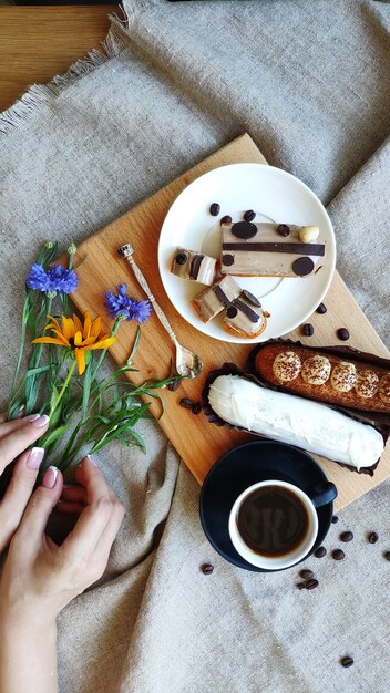 Vue de dessus sur les mains féminines avec des fleurs d'été près d'une tasse de café noir et servi éclairs