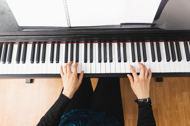 Vue de dessus des mains de femme jouant du piano en lisant des partitions.