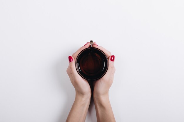 Vue de dessus des mains d&#39;une femme avec une manucure rouge tenant une tasse de thé