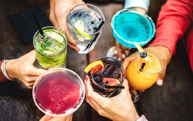 Vue de dessus des mains des gens grillant des boissons fantaisie multicolores Jeunes amis s'amusant à boire des cocktails à l'happy hour Concept de fête de rassemblement social sur filtre vif Faible profondeur de champ