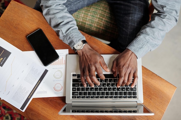 Vue de dessus des mains d'un jeune homme noir sur un clavier d'ordinateur portable