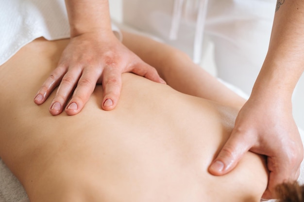 Vue de dessus des mains d'un masseur masculin avec des mains fortes massant professionnellement les omoplates et les épaules Belle jeune femme nue avec une peau parfaite recevant un massage relaxant