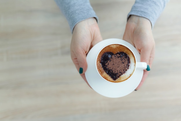 Vue de dessus des mains tenant une tasse de café blanche. coeur imprimé sur le café