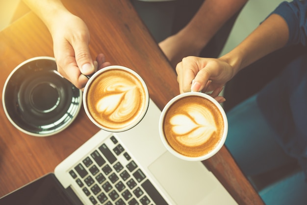 Vue de dessus des mains tenant la tasse de café sur le bureau de travail avec un ordinateur portable