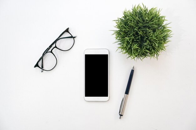 vue de dessus de la maquette smartphone, verre, stylo et plante sur fond de couleur blanche