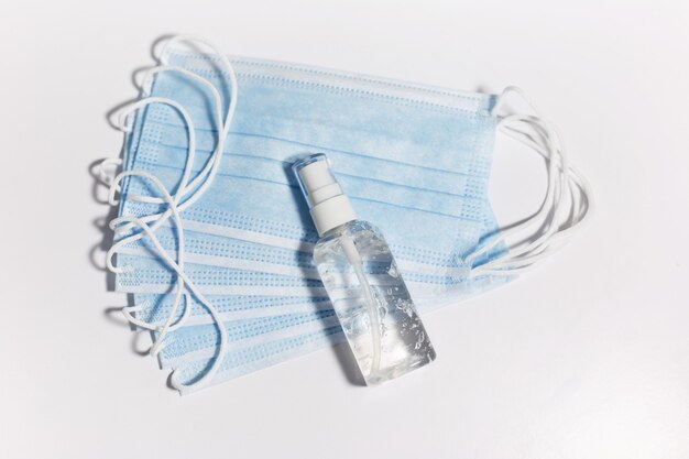 Vue de dessus des masques médicaux contre la grippe et petit flacon distributeur portable avec gel antiseptique désinfectant pour les mains