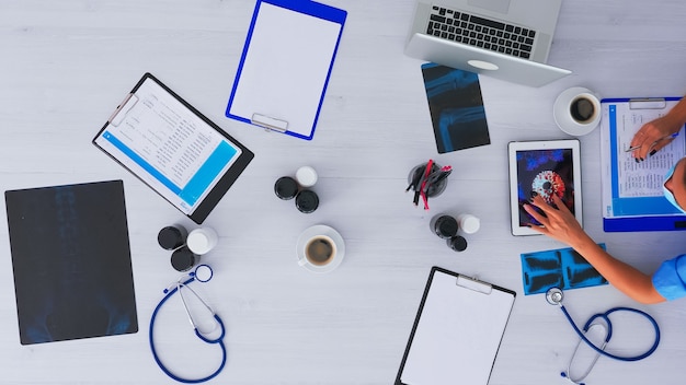 Vue de dessus d'un médecin faisant des recherches sur le virus à l'aide d'une tablette, prenant des notes assis sur un bureau dans une clinique médicale avec radiographie et technologie numérique