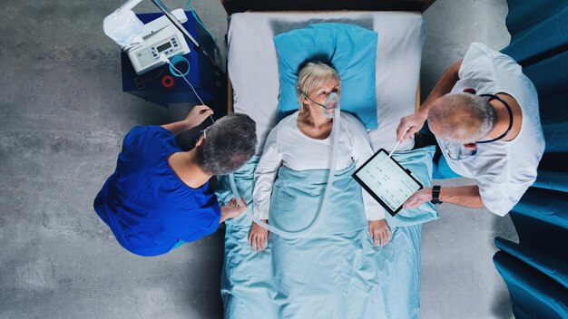 Photo vue de dessus des médecins et du patient covid19 infecté avec un masque à oxygène au lit à l'hôpital