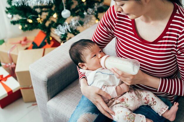 vue de dessus de la mère asiatique nourrit son jeune enfant. bébé affamé buvant du lait de bouteille dans les bras de sa mère. style de vie authentique