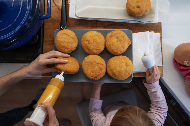 Vue de dessus d'une mère remplissant des beignets végétaliens fraîchement frits avec de la confiture, avec sa petite fille l'aidant.