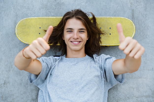 Vue de dessus d'un mignon jeune garçon adolescent passer du temps au skate park, portant sur une planche à roulettes à une rampe, montrant les pouces vers le haut