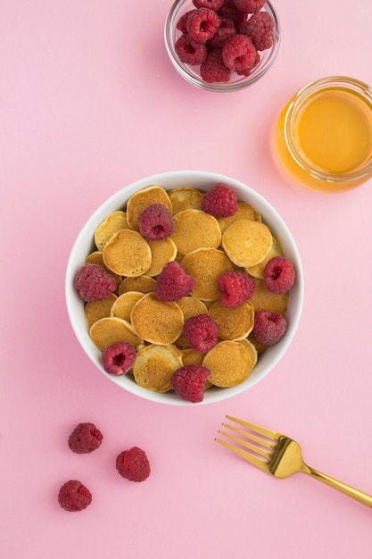 Vue de dessus de mini crêpes aux framboises dans le bol blanc sur la surface rose