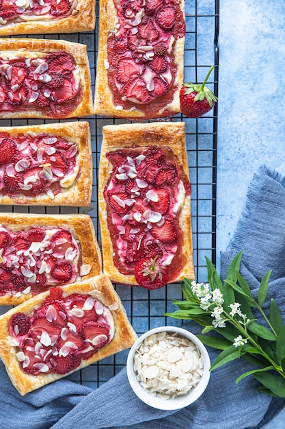 Photo vue de dessus de mini tartes feuilletées au fromage à la crème et aux fraises décorées d'amandes. fond de béton bleu.