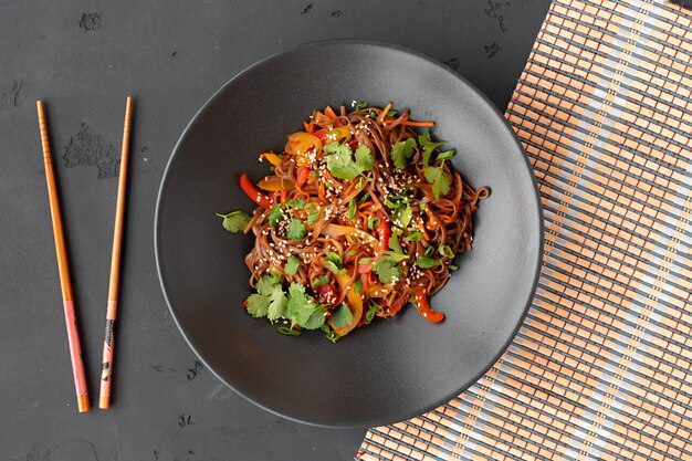 Vue de dessus des nouilles au wok avec des légumes et de la viande dans un bol sur une surface grise