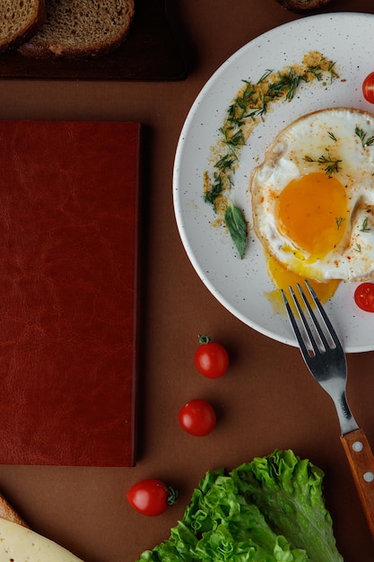 Vue de dessus de l'oeuf au plat avec tomate et aneth avec fourchette et tomates laitue avec planche à découper sur fond marron