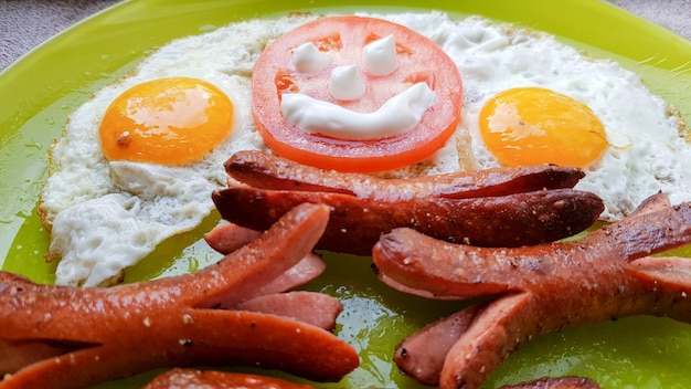 Vue de dessus d'œufs au plat et de saucisses sur une assiette verte, servant le petit-déjeuner pour le bébé.