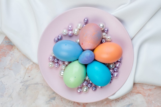 Vue de dessus des oeufs de pâques colorés dans une assiette avec des perles sur fond clair concept coloré de Pâques horizontal vacances printemps