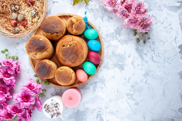 vue de dessus des oeufs de pâques colorés avec du pain de vacances et des gâteaux à l'intérieur du plateau sur une surface blanche