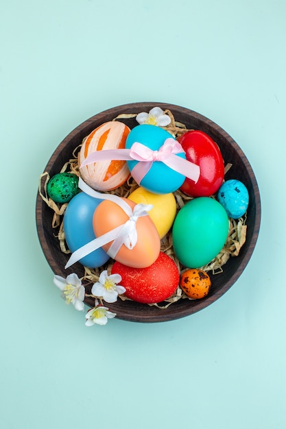 vue de dessus des oeufs de pâques colorés à l'intérieur d'une assiette en bois sur une surface bleue