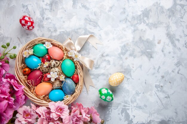 Vue de dessus des oeufs de pâques colorés à l'intérieur du panier sur une surface blanche printemps coloré fleur de pâques concept orné de vacances