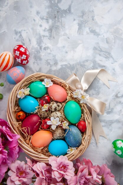 Vue de dessus des oeufs de pâques colorés à l'intérieur du panier sur une surface blanche printemps fleur de pâques colorée concept orné