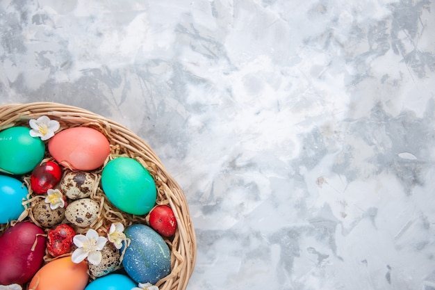 Vue de dessus des oeufs de pâques colorés à l'intérieur du panier sur une surface blanche vacances de printemps pâques concept coloré orné de place libre