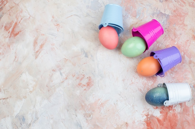 Vue de dessus des oeufs de pâques colorés à l'intérieur de petits paniers séparés sur fond clair printemps orné de vacances horizontales colorées