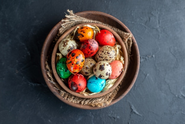 vue de dessus des oeufs de pâques colorés à l'intérieur d'une plaque brune sur une surface sombre