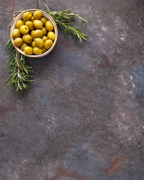 Vue de dessus des olives vertes dans un bol avec du romarin.