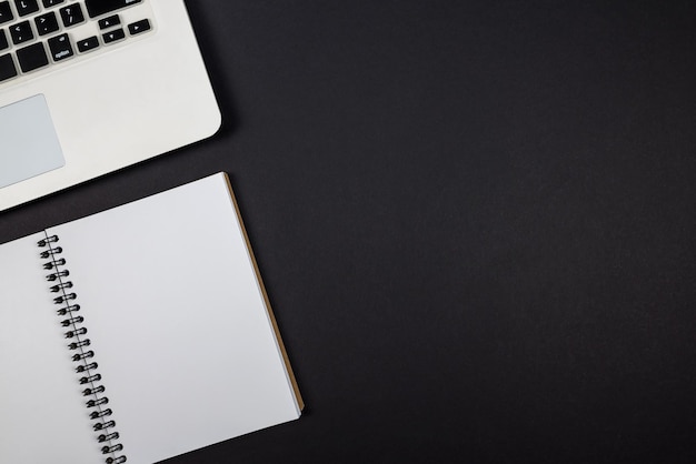 Vue de dessus d'un ordinateur portable blanc avec un bloc-notes blanc vierge sur un espace de copie de fond noir isolé