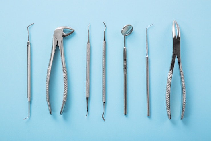 Photo vue de dessus des outils dentaires sur table bleue dans la clinique des dentistes: miroir dentaire, explorateurs, pinces.