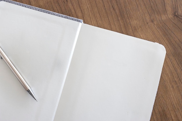 Vue de dessus d'une page de cahier ouvert vierge et d'un crayon sur fond de table en bois au bureau